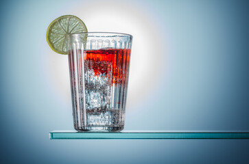 Partygetränk Glas Wasser mit einer dekorierten Zitrone sowie eingefärbte Flüssigkeit mit Eiswürfel, Glass of sparkling water on the blue background, 