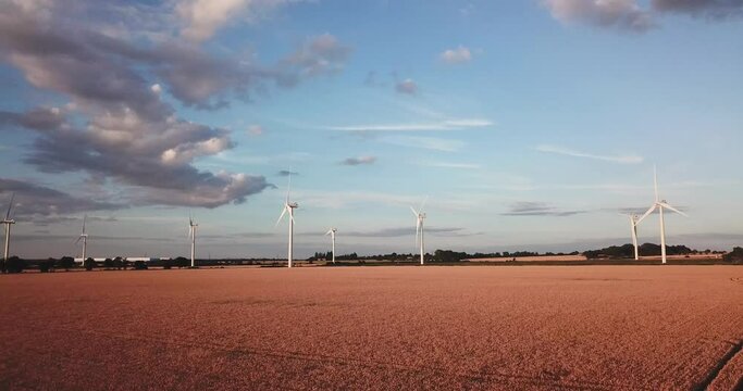 medium angle drone shot moving forwards towards wind turbines over a field during a stunning golden hour sunset in Bedfordshire, uk on a sunny summers day
