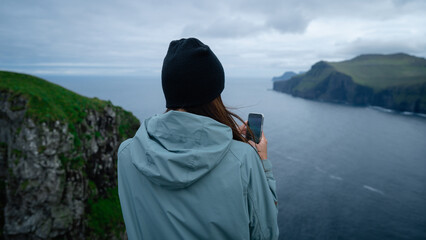 Woman tourist use mobile phone, take photo or record video of landscape of beautiful cliff's edge...