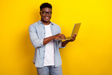 Photo of nice millennial brunet guy type laptop wear eyewear jeans shirt isolated on yellow color background