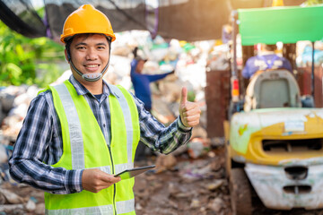 Asian  foreman thumbs up and holding tablet and looking at recycle waste factory with a forklift on...