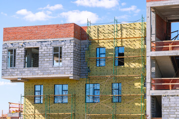 Frame of a building under construction. Construction of buildings in the city. Technologies in the construction of houses. Cladding and insulation of walls on rafters.