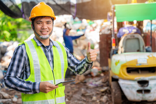Asian  foreman thumbs up and holding tablet and looking at recycle waste factory with a forklift on the background.