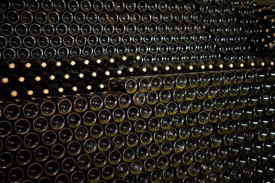 Many glass wine bottles on wine shelves. interior in distillery. Row of Stacked wine bottles in cellar to ferment the wine.