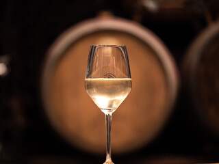 White wine in a glass with wooden barrel in the background - obrazy, fototapety, plakaty