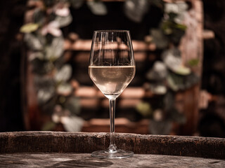 Glass with white wine and a small decorated barrel in the background - obrazy, fototapety, plakaty