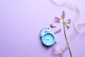 Beautiful tulip, ribbon and alarm clock on violet background, flat lay with space for text....