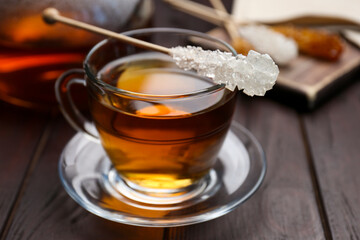 Stick with sugar crystals and cup of tea on wooden table, closeup