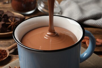 Pouring yummy hot chocolate into mug on table, closeup