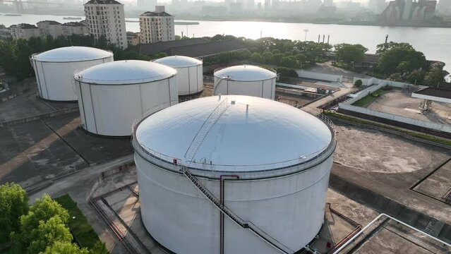 Oil storage tanks in rows along the riverside. Drone aerial view. Oil storage tanks in the sunset time, flying over the tanks along the river.  Industry, business, economy concept b-roll footage.