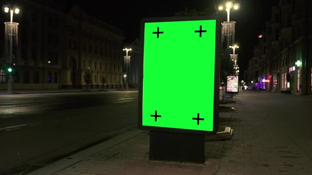 Vertical billboard with a green screen and track Markers on a European city street at night. Mock up concept to add your slogan, logo, advertisement or other image. Handheld Shooting.