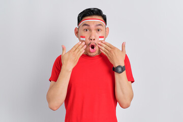 Shocked young Asian man celebrating Indonesian independence day looking at camera with open mouth isolated on white background