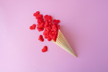 Creative photo of empty waffle cones with scattered red hearts on a pink background. The concept of love, summer, spring