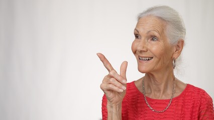 Portrait of elderly mature woman smiling showing area to side, giving thumbs up isolated on solid white background in studio.