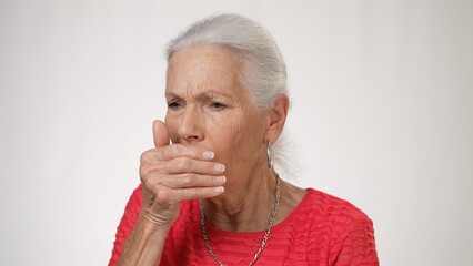 Portrait of pretty elderly woman coughing on solid white background.
