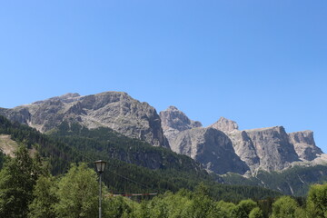 Fototapeta na wymiar Coravara, Italy-July 16, 2022: The italian Dolomites behind the small village of Corvara in summer days with beaitiful blue sky in the background. Green nature in the middle of the rocks. 
