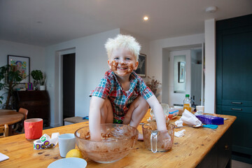 A young boy with hands and face covered in chocolate after helping in the kitchen to bake a cake