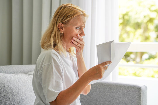 Disappointed young woman sit on sofa at home read bad news in a letter eviction notice, bankruptcy, bank debt, electricity bill. Worried woman reading negative news in a letter at home