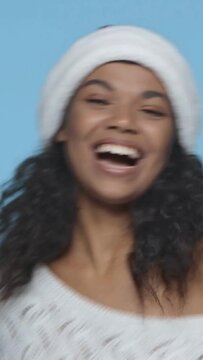 vertical video of happy african american woman in santa hat dancing isolated on blue