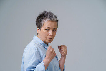 Frightened woman with hands put in fists. Senior woman with grey hair pose as boxing fighter about...