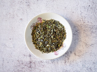 Plate filled with dried green tea leaves on a white table.