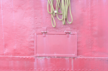 rosafarbener Ausschnitt einer Bordwand eines Schiffes mit einem Tampen