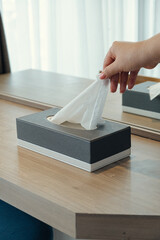 Closeup woman hand picking white tissue paper from tissue box on wooden table