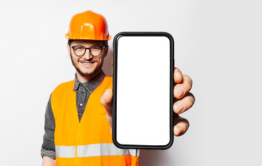 Studio portrait of construction worker holding smartphone with blank screen on white background....