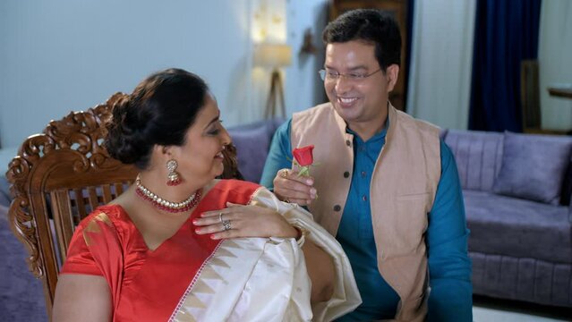 A middle-aged handsome Bengali couple romancing - putting a rose on his wife's hair  romantic couple  festive mood. A newly married Bengali couple together in the living room at home - quality time...