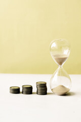 hourglass and stack of coins on table, 