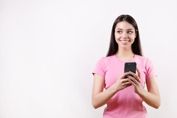 Naklejka premium Portrait of young brunette woman wearing pink t-shirt texting on the phone over isolated white background. Joyful female holding a smartphone. Copy space for text, background, close up.