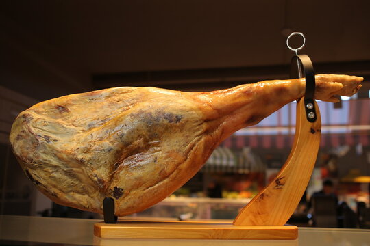 Jamon serrano. Traditional Spanish ham Jamon - whole leg of dried pork meat on a wooden stand. Pork leg on table. Traditional Spanish ham in restaurant or store interior. jamon on stand. Soft focus.