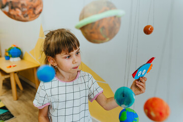 Little girl playing with paper spaceship learning Solar system planets
