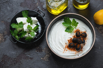 Greek feta dip topped with black olives and paprika, elevated view on a brown stone background, horizontal shot