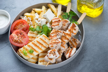 Grilled halloumi, chicken souvlaki, greek-style fries with feta and tomatoes, horizontal shot on a grey concrete surface