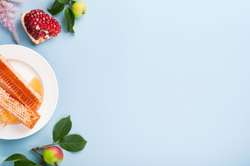 Rosh Hashanah. Honey jar, honeycomb, apple and pomegranate on simple blue background. Jewish New Year holiday greeting card. Rosh Hashanah holiday attributes. Space for text