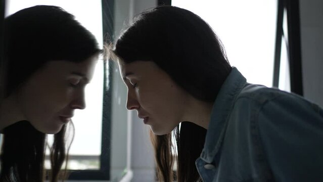 Anxious woman looking at her own reflection at bathroom mirror feeling regret and preoccupation