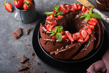 Dark Chocolate Bundt Cake with Ganache Icing and strawberry on dark stone or concrete table background. Festive cake. Selective focus