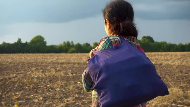 A young woman with a bag is walking along a country road. The girl returns home along a rural road with a bag in her hands. Camera movement behind the subject. The concept of loneliness, hopelessness.