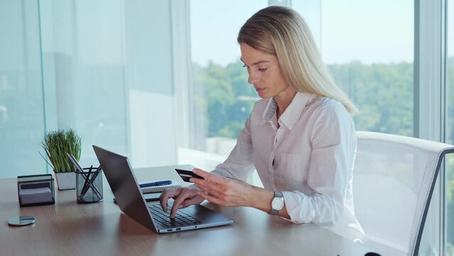 Young business woman entering credit card number on laptop, paying utility bills. Female hands holding Credit Card makes purchase on web site, use e-bank app sit at table indoor. Easy secure payment.