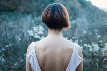 Autumn portrait of a girl with short hair outdoors, rear view. portrait of a woman with a bare back between her dress looking at the horizon.conceptual photography dramatic atmosphere of autumn winter