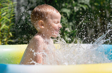 A hot summer day. Children swim and splash in the pool. A happy little boy smiles at the camera. Splashes of water are flying in all directions. The concept of summer holidays with children.