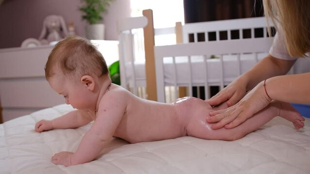 Sweet newborn baby from the back and bottom side view. Mom applies the cream to the baby's skin. Health and skin care, baby development concept. Slow motion 4K video