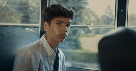 Pensive Indian boy sitting at school bus window closeup. Pupil looking camera.