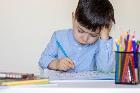 preschooler boy sits on school desk with thinking face emotional support marker with head.child drawing on paper with colorful pencils,markers.back to school.isolated cute adorable boy in blue shirt