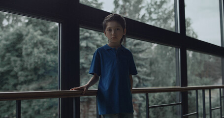 Sad boy standing alone at panorama window. Teen schoolchild feeling loneliness.