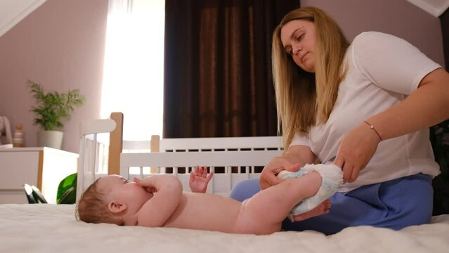 loving mother puts a diaper on a baby lying on a bed in a nursery