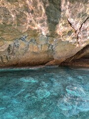 Amazing rock with light reflection in mysterious sea cave grotto. Blue clear water and coastal cliffs.