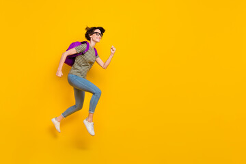 Fototapeta na wymiar Full length photo of sweet excited lady wear striped t-shirt spectacles backpack running fast empty space isolated yellow color background