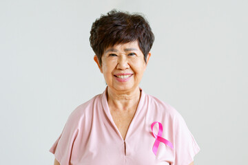 Portrait of middle-aged Asian woman in pink shirt with pink ribbon smiling on gray background for...